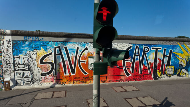 A surviving section of the Berlin Wall, with artistic graffiti reading "Save the Earth," behind an iconic red "do not walk" Ampelmann traffic signal