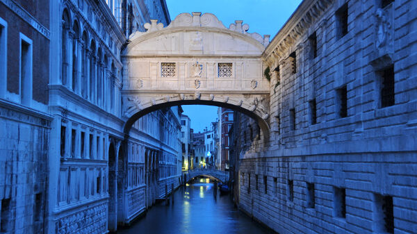 Venice's Bridge of Sighs, lit up in the evening, over a blue canal