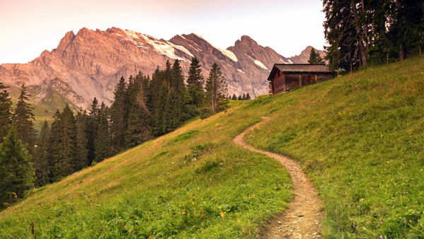 Golden-hour sunlight on an alpine ridge at the southern end of Switzerland's Lauterbrunnen Valley, with a hillside wooden hut in the middle ground