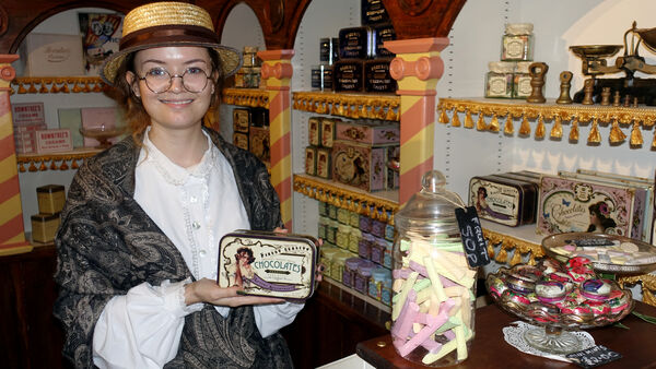 A purveyor in Victorian dress holding up some "sweets" for sale in a 19th-century shop inside the Castle Museum in York, England