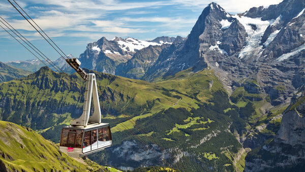 Cable car carrying passengers up the mountainside above Mürren, Switzerland, with the green Männlichen ridge and rocky Eiger peak in the backgroundround