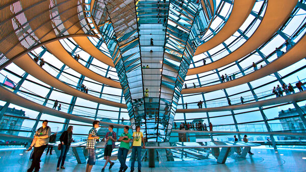 Visitors climbing the spiral ramp inside the Reichstag's glass dome, circling a cone of mirrors while peering across the rooftops of Berlin