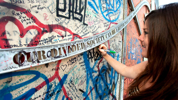 A woman uses a pen to add to the writing on Belfast's "Peace Wall"