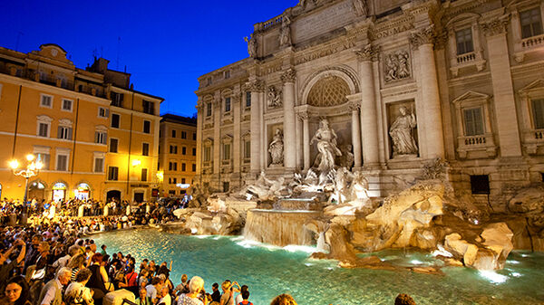 People crowding around Rome's Trevi Fountain at dusk