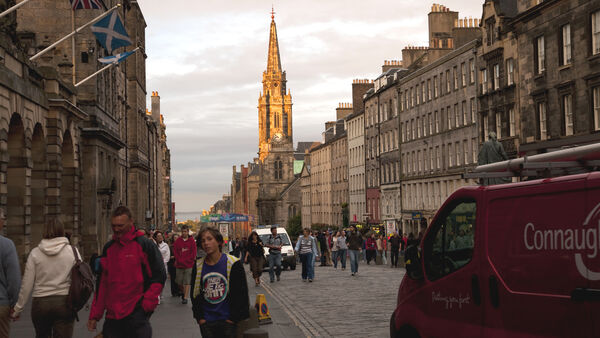 People fillling the sidewalks (and streets) of Edinburgh's Royal Mile under the spire of Tron Kirk, lit by low afternoon light