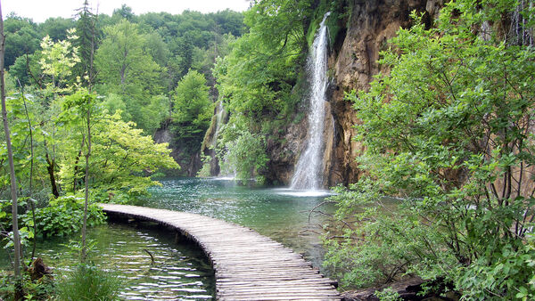 A waterside walkway leading past a waterfall in Plitvice Lakes National Park, Croatia