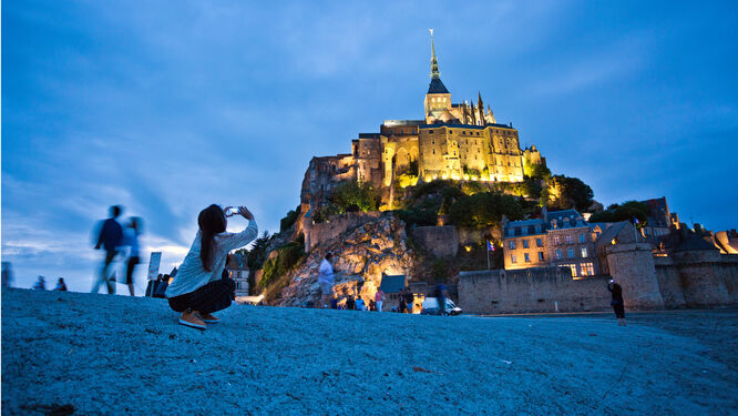 A visitor takes a photo of Mont St-Michel, France, while it's floodlit at dusk
