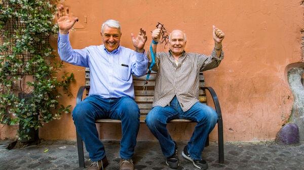 Two smiling older local men on bench, Italy