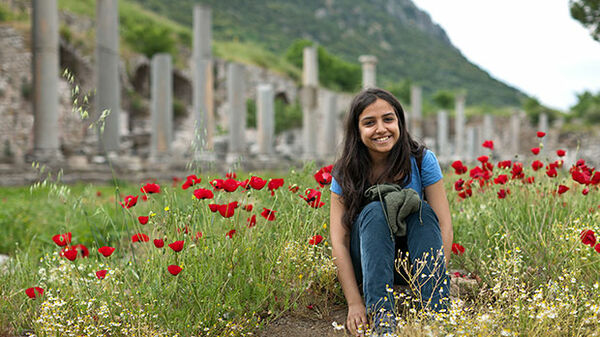 Smiling girl sitting in poppies, Ephesus, Turkey