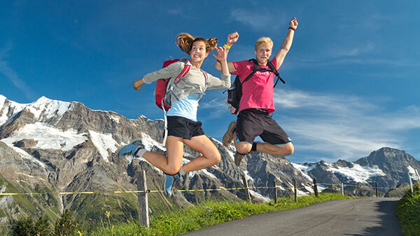 Young gal and guy leaping in front of mountains, Switzerland