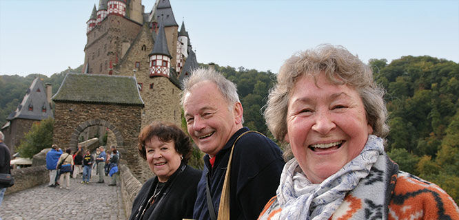 three people posing in front of burg eltz castle in germany