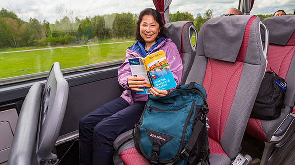 Smiling woman on tour bus with RSE guidebook and bag, Poland