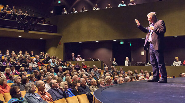 a man standing on stage speaking to a crowd of people