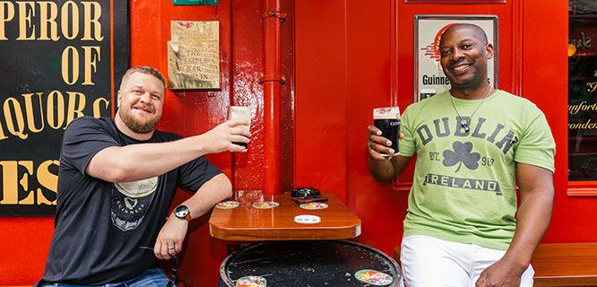 two men toasting with beer in front of a red pub