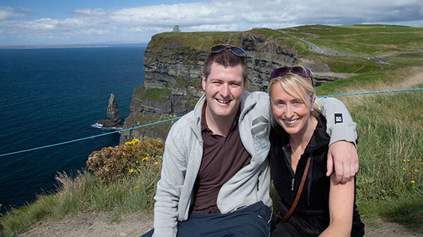 man and woman sitting with cliffs and water behind them