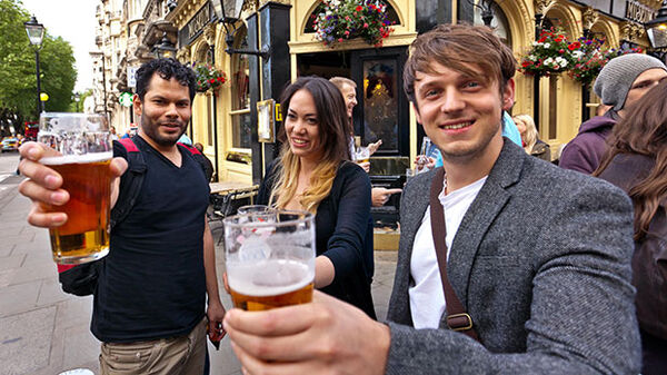 two young men and a young woman toasting with glasses of beer