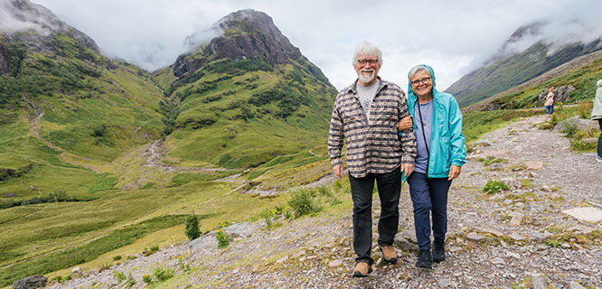 man and woman walking on rocky path with mossy hills and mist