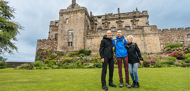 two men and a woman in front of stone castle