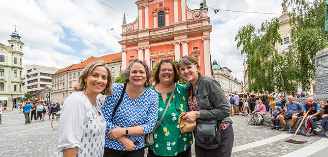 four women standing in front of a pink ornate building
