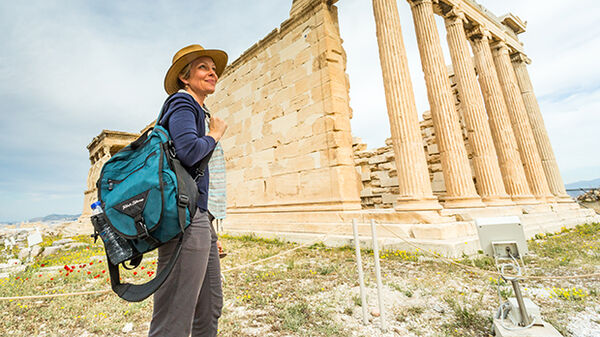 A woman stands in front of Greek ruins